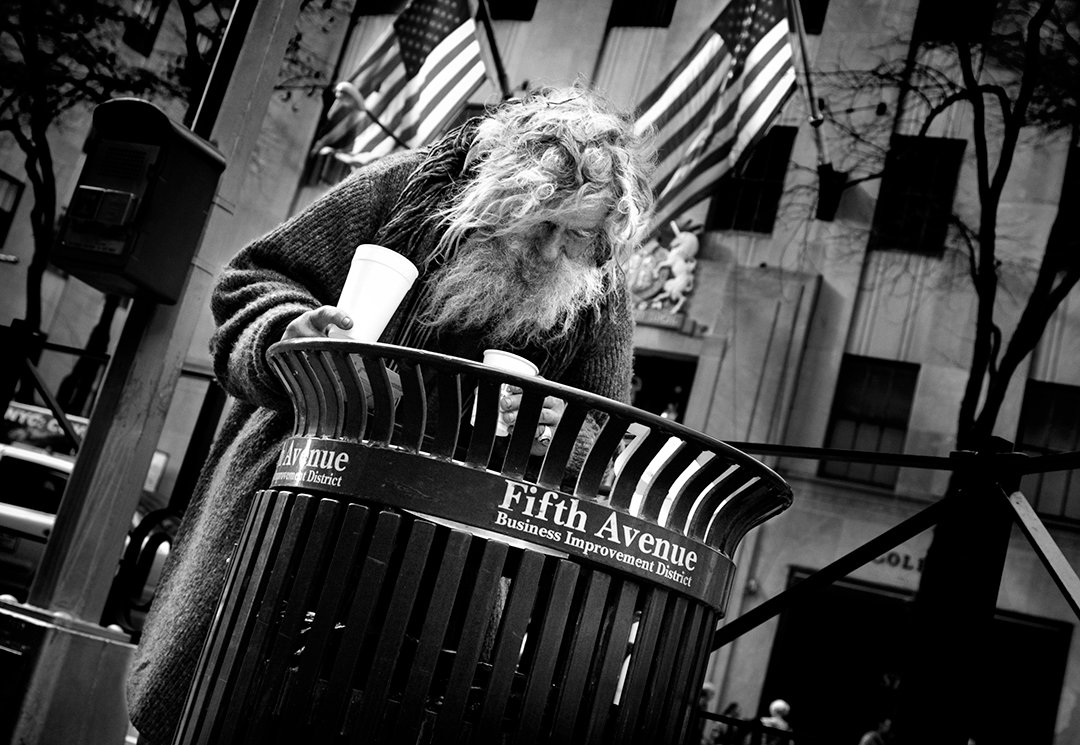 A person leaning over a litter bin with a cup in their hand.
